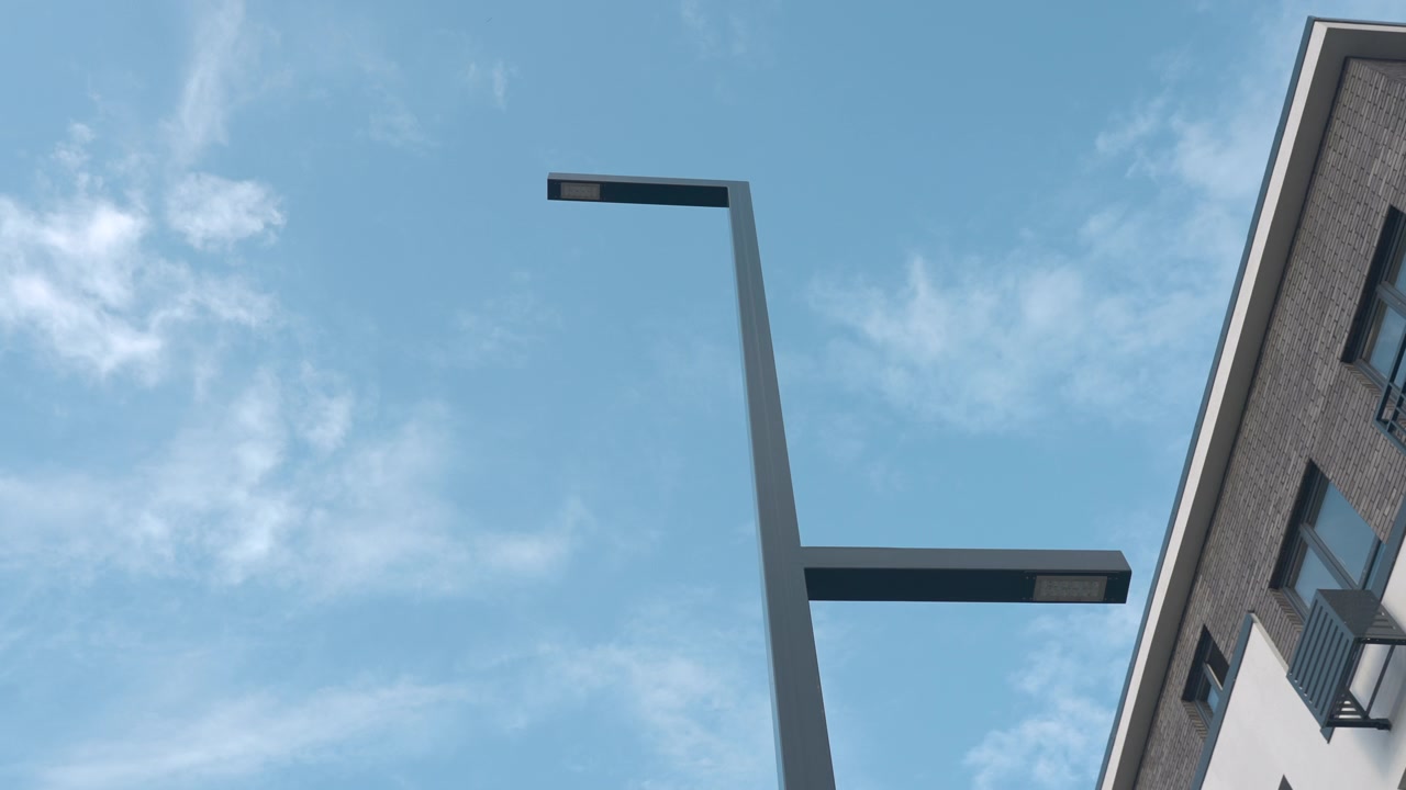 Eine hohe Metall-Straßenlaterne ist von unten vor einem klaren blauen Himmel mit leichten Wolken zu sehen, was eine minimalistische urbane Szene mit viel Freiraum schafft.