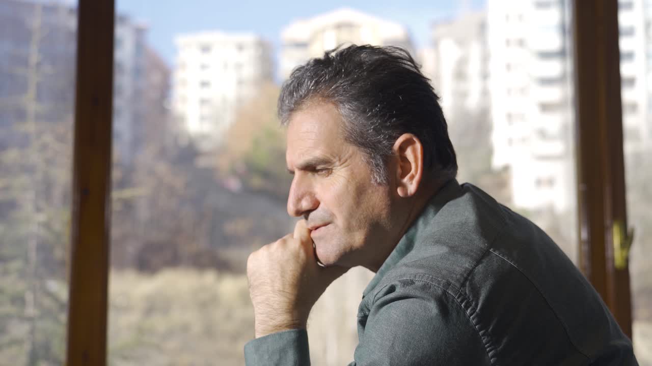 un uomo maturo premuroso seduto vicino alla finestra e che pensa. un uomo maturo premuroso, triste e addolorato.