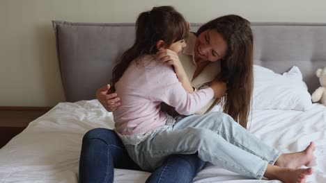hija feliz y madre cosquilleándose la una a la otra divirtiéndose en el interior