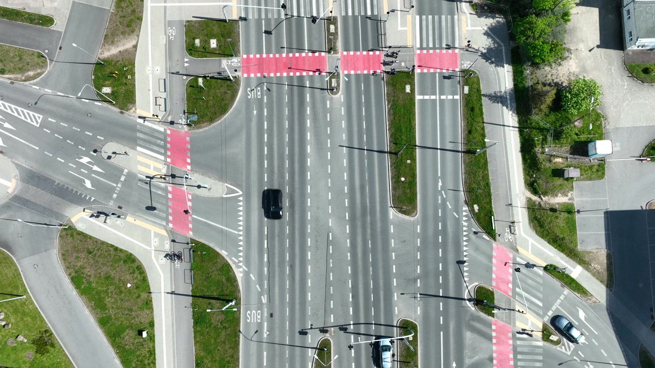 High angle top down shot of a modern urban road junction in Gdynia featuring red bicycle lanes and pedestrian crossings with light traffic on a sunny day.