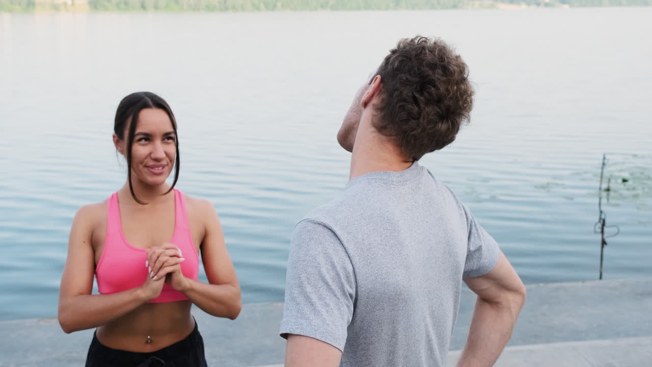 feliz pareja deportiva calentándose y estirándose cerca del río