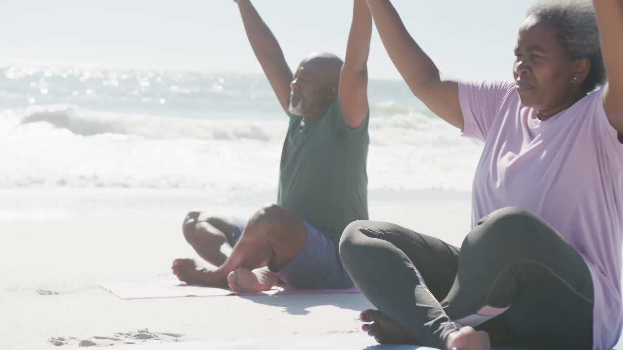 Casal idoso afro-americano feliz praticando yoga e meditando na praia, em câmera lenta