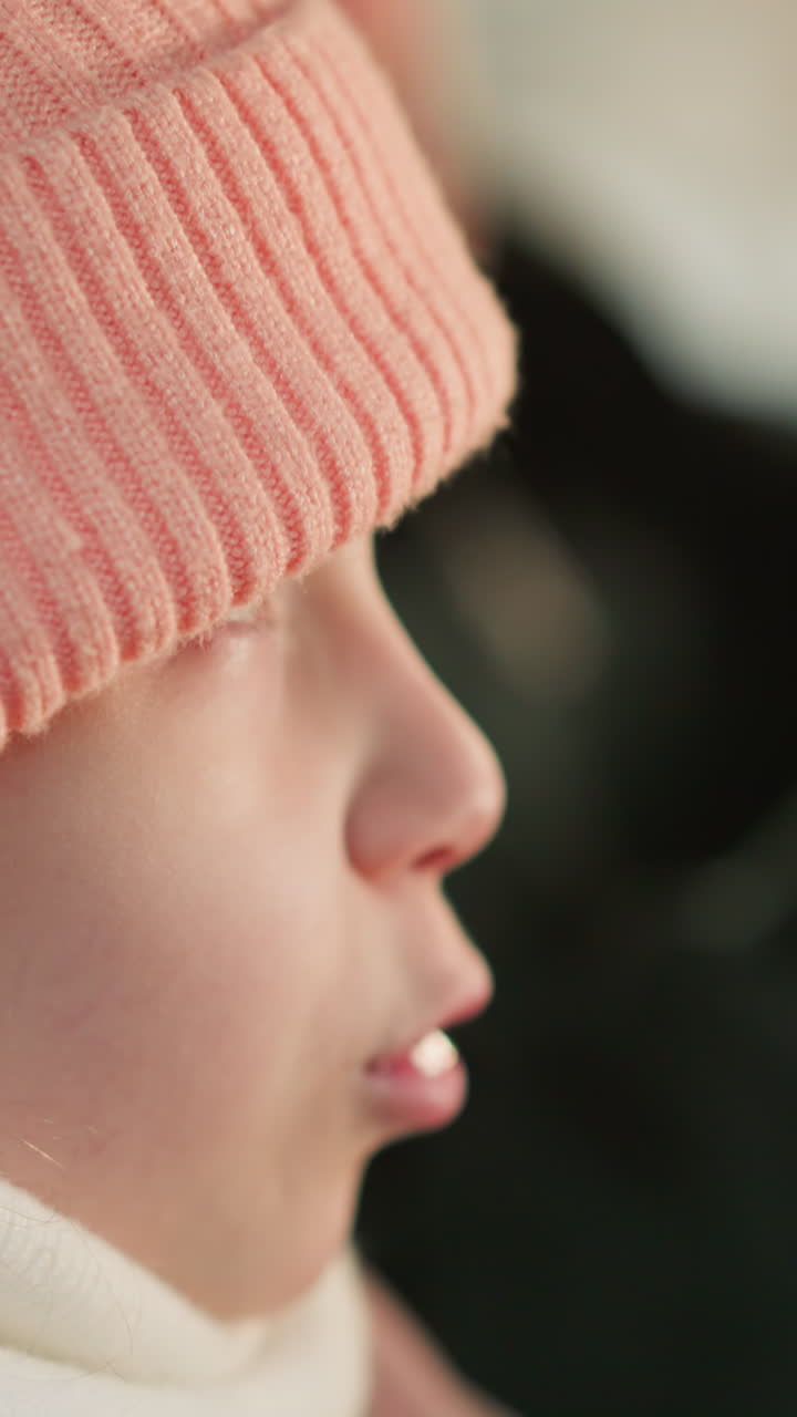 un primer plano de una joven con un gorro y una chaqueta rosas, sentada dentro de un coche. su expresión está enfocada, con los labios ligeramente apretados mientras mira hacia adelante