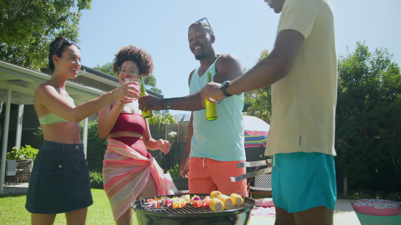Diverse friends enjoying barbecue by pool, grilling food and drinking on sunny day