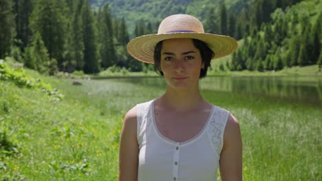 young woman in a straw hat stands by a serene forest lake on a sunny summer day