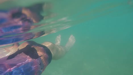 action cam pov of man on sea water surface doing horizontal back float next to cliffs