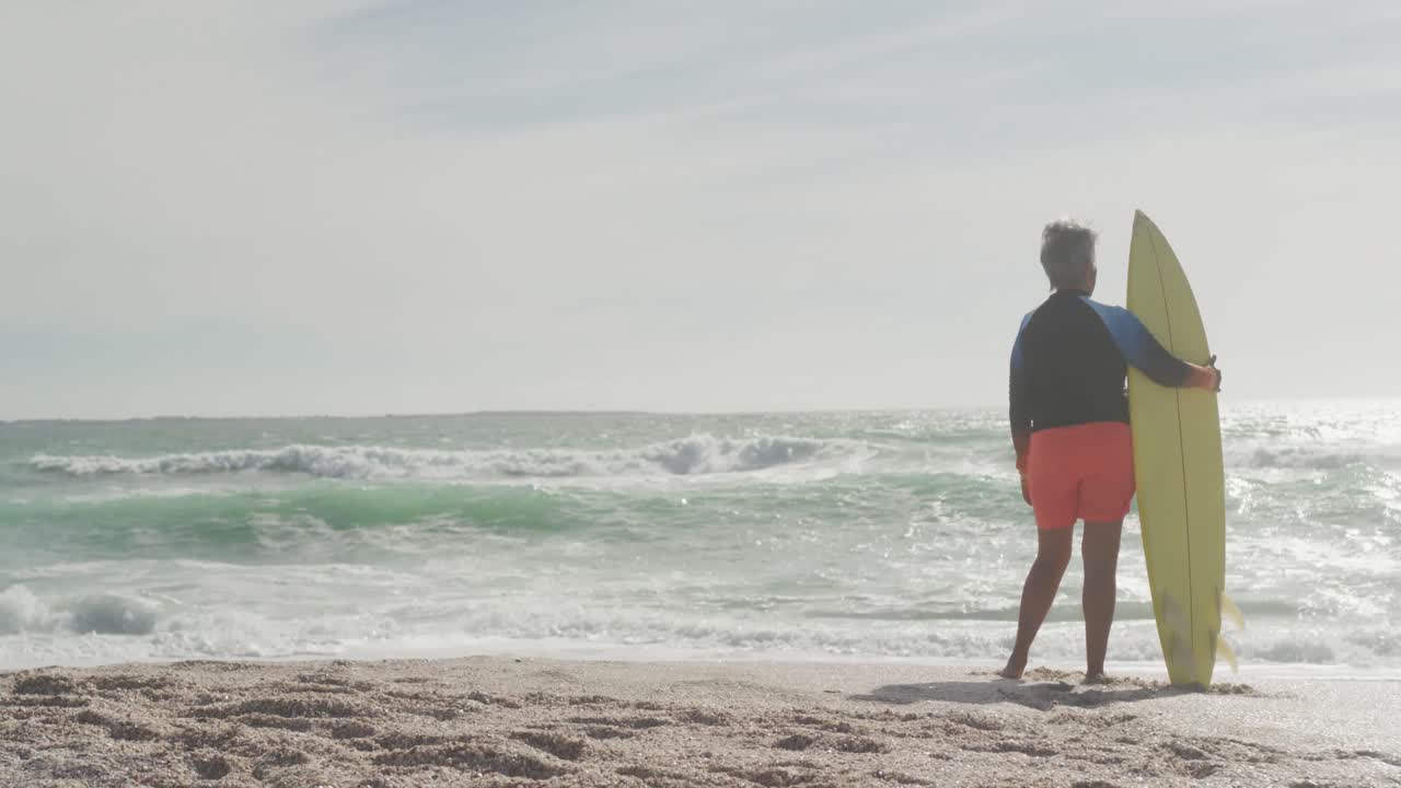 서프보드와 함께 해변에 서 있는 수석 히스패닉 여성의 뒷면