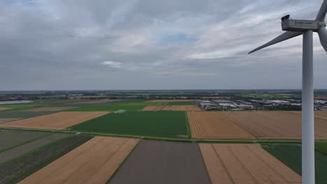 wind turbine spins above vast farmlands under a cloudy sky, aerial view