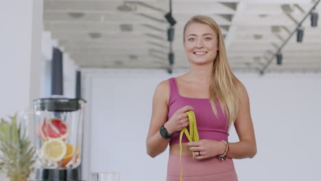 a young beautiful caucasian woman smiles at the camera holding the tape measure - a healthy living concept