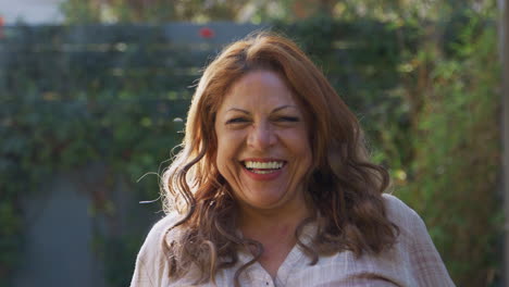 portrait of smiling senior hispanic woman  in garden at home against flaring sun