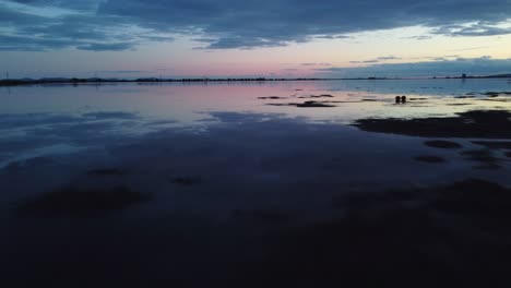 Spectacular-low-aerial-shot-of-still-calm-water-at-sunset,-sky-reflection