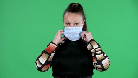portrait elderly woman looking at the camera and puts the medical mask. brunette granny in black dress on green screen at studio. close up
