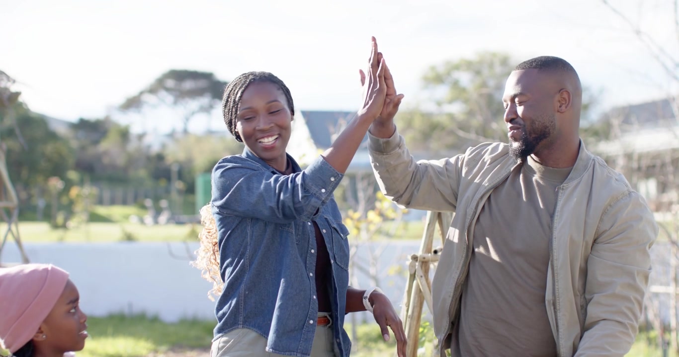 Family clapping, celebrating child wearing pink beanie raising hands for high-fives in garden