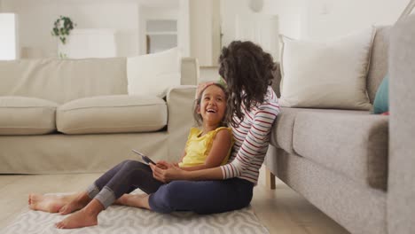 madre y hija hispanas felices sentadas en el suelo usando una tableta