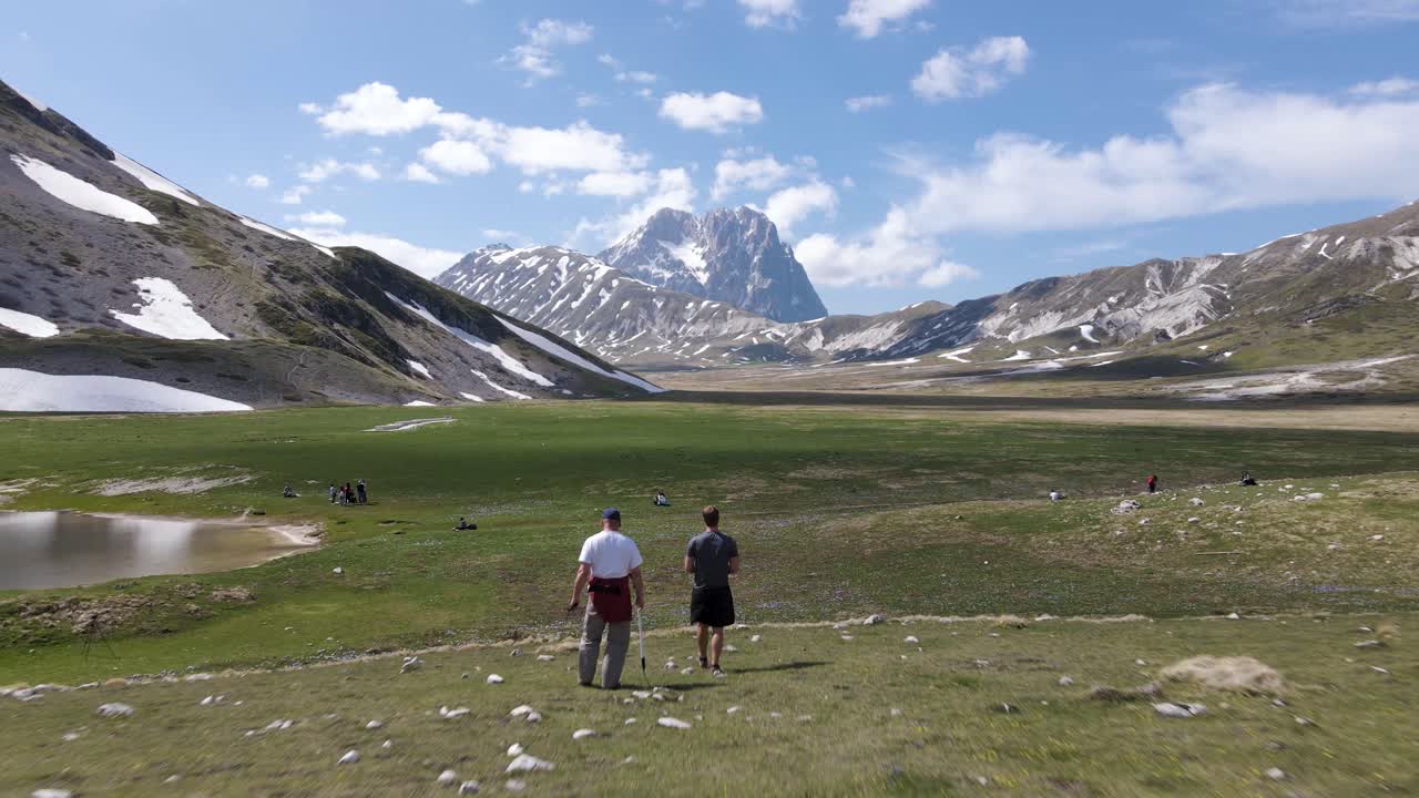 Wide angle drone shot of a national park in a valley with mountains in the distance, with many people enjoying the views and having a picnic located in the region of Abruzzo in Italy