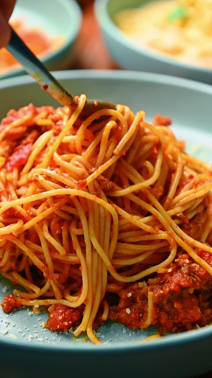 Spaghetti alla bolognese avvolti sulla forchetta con ragù di carne al pomodoro. Primo piano di pasta con sugo rosso alla bolognese e foglia di basilico su piatto blu.