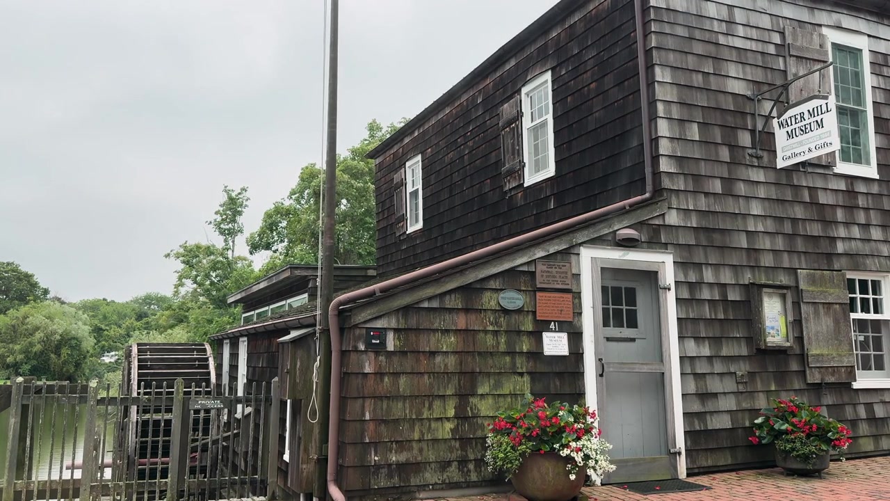 Historic wooden water mill museum exterior with waterwheel and garden planters
