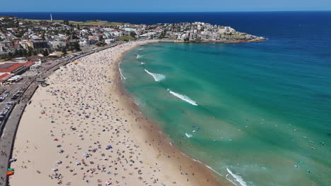 wide drone shot of bondi beach with crowds soaking up the sun and swimming in the crystal-clear waters. aerial shot, new south wales.