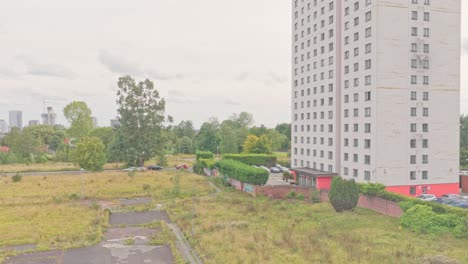 tall residential tower stands next to an overgrown vacant lot and surrounding greenery in salford, england, captured in descending aerial shot
