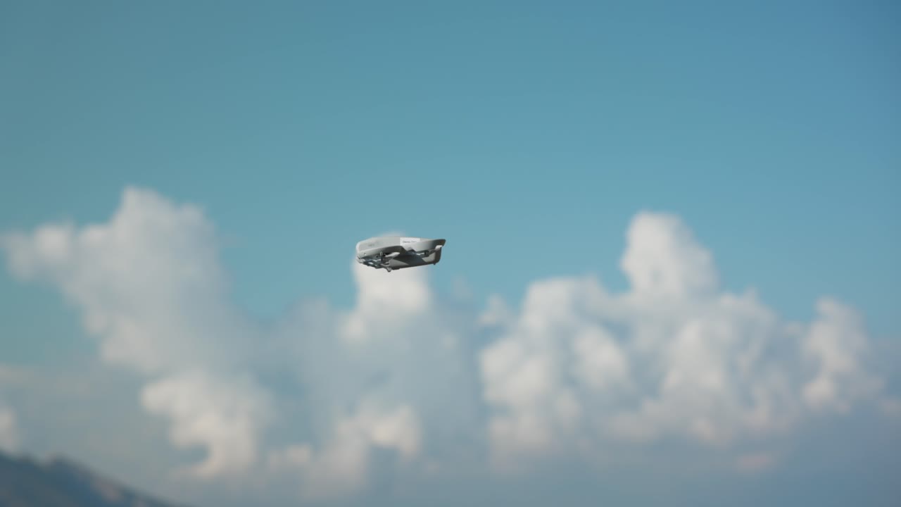 A DJI Neo drone soars through a clear blue sky above a rocky landscape, showcasing modern technology and exploration potential.