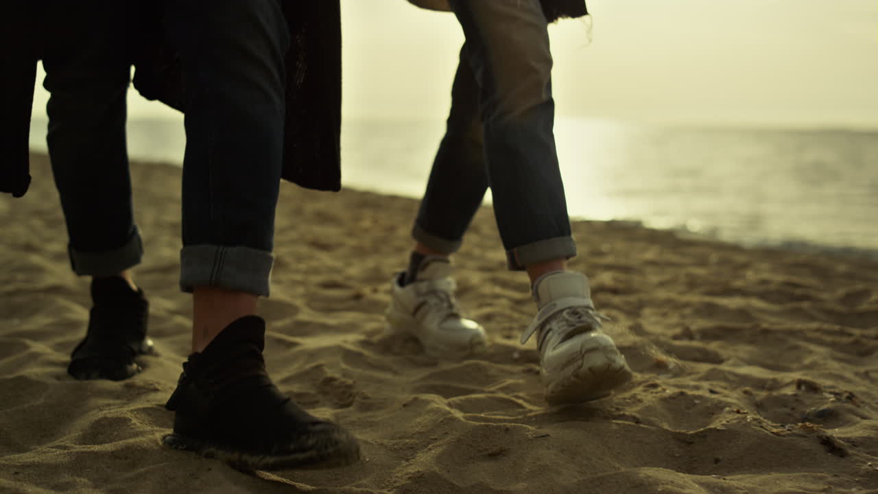 해가 지는 해변에서 모래 해변을  ⁇ 는 사람들의 다리. 해변에 발을  ⁇ 는 커플.