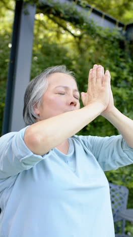 Vertical video: Meditating with hands in prayer position, senior woman outdoors focusing on mindfuln