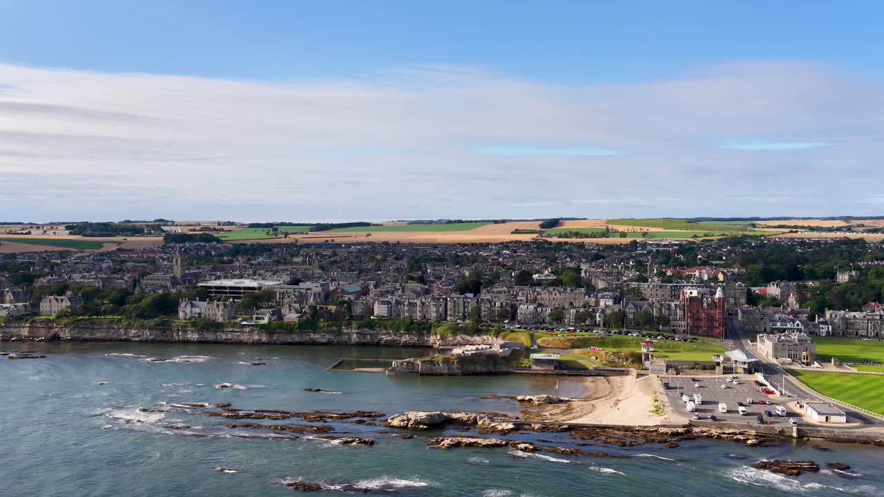 Smooth drone aerial reveals St Andrews coastline, historic buildings, golf course, and seaside under daylight