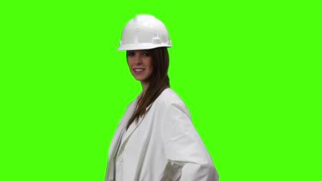 Joven-Mujer-Rubia-Marrón-Con-Bata-Blanca-De-Laboratorio-Médico-Y-Sombrero-Duro-Mira-Sonriendo-A-La-Cámara,-Luego-Se-Enfrenta-A-La-Cámara-Y-Cruza-Los-Brazos