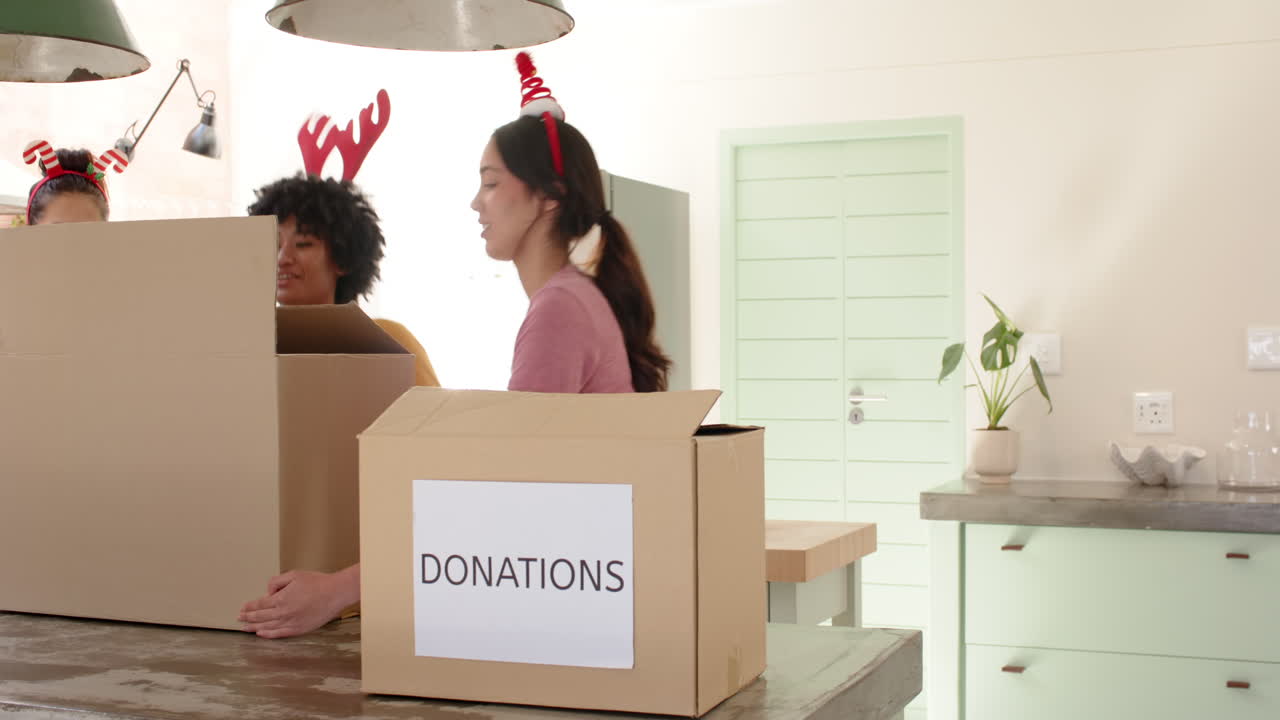Christmas time, Women friends wearing festive headbands packing donation boxes in cheerful kitchen