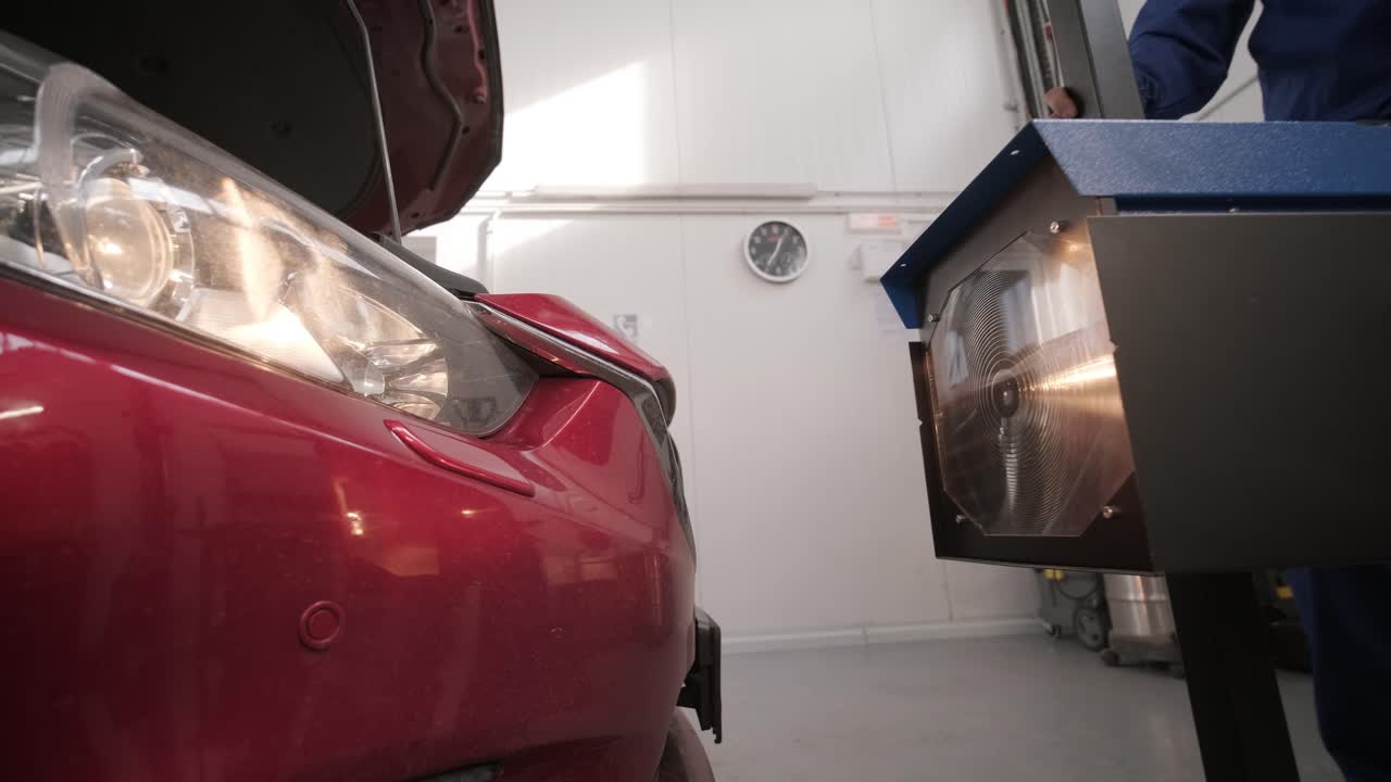 노동자는 자동차 조명 시스템의 헤드라이트를 확인하고 조정합니다.