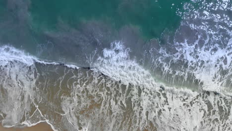 Toma-Aérea-De-Arriba-Hacia-Abajo-Volando-A-Lo-Largo-De-Una-Playa-Con-Las-Olas-Rodando-Durante-La-Tarde