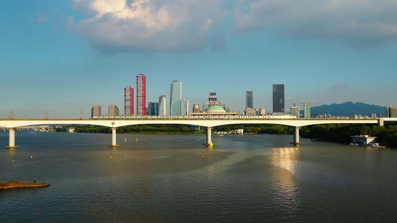 Golden hour sunset light reflects on a subway train passing Dangsan Bridge over the Han River, with the National Assembly Building and Yeouido's skyscrapers creating the iconic Seoul skyline - aerial