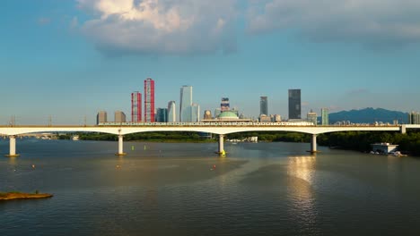 golden hour sunset light reflects on a subway train passing dangsan bridge over the han river, with the national assembly building and yeouido's skyscrapers creating the iconic seoul skyline - aerial