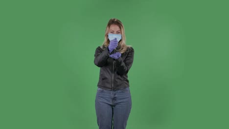 코로나 바이러스의 확산을 막기 위해 의료 보호 얼굴 마스크를 입은 아름다운 젊은 여성의 초상화. 검은 재과 청바지를 입은 느슨한 머리카락을 가진 금발이 스튜디오의 녹색 스크린에 건강 보호 코로나