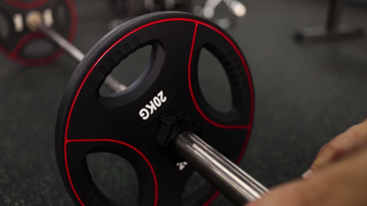 Male hands fix heavy weight plate on barbell in gym