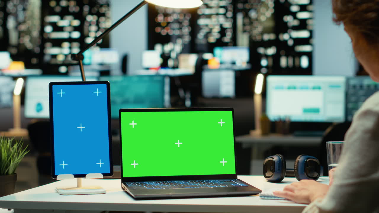 Executive manager at desk uses green screen on laptop and blue screen on tablet