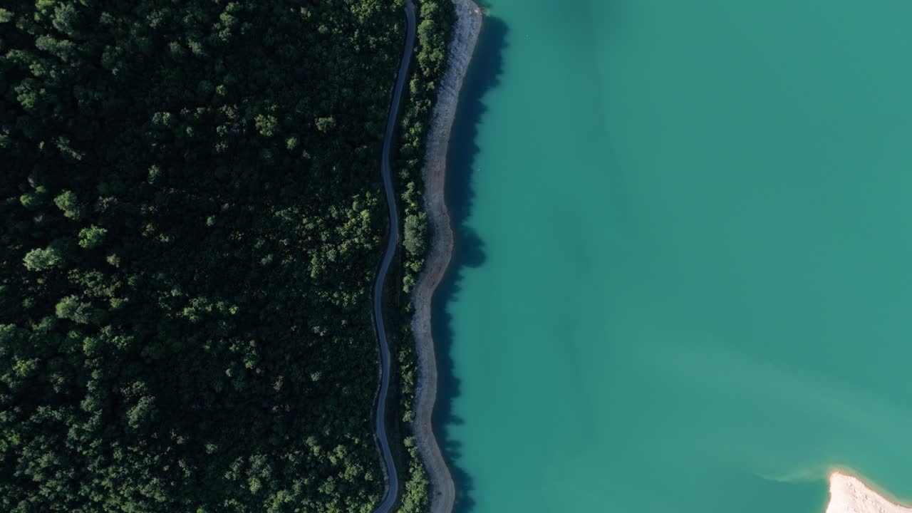 Birdview flying along the coastel road of the turquiose lake Pivsko near Pluzine surrounded by green forrests and mountains in Montenegro during august summertime