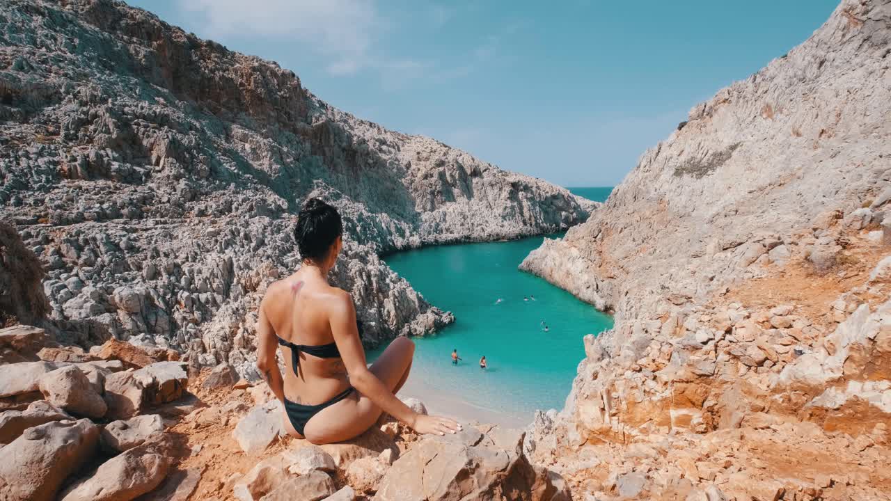 una mujer sentada en la cornisa, observando una bahía turquesa