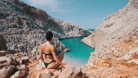 a woman sitting on the ledge, overseeing a turquoise bay