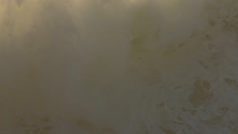 gran ola rompiendo en la playa de nazare con spray haciendo una neblina en el fondo