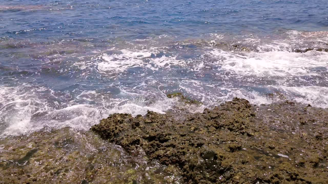 Waves crash on volcanic rocks off Tenerife coast, creating a serene view