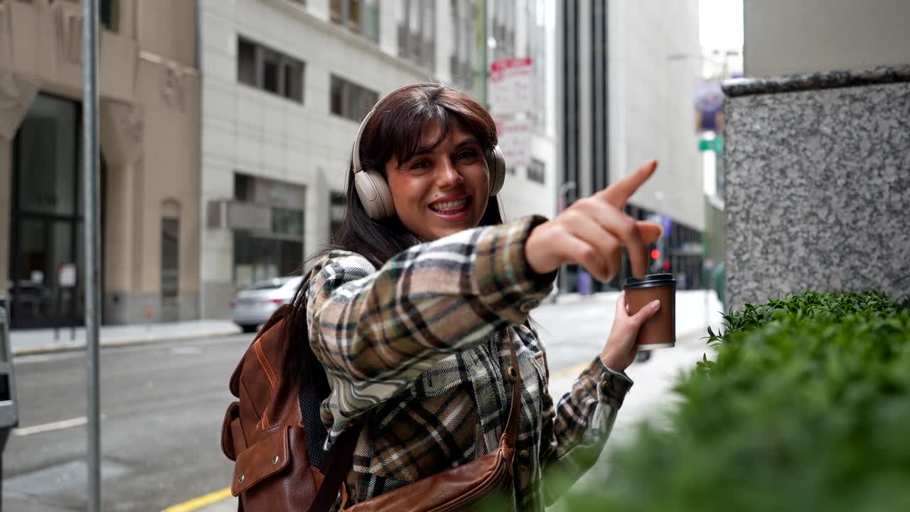 Joven mujer bailando y cantando con auriculares en una calle de la ciudad