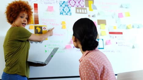 female executives discussing over sticky notes on whiteboard