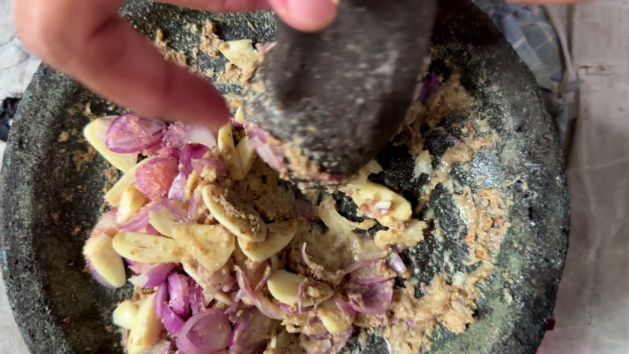 Gewürze und Zwiebeln werden manuell in einem Steinmörser zerkleinert. Authentische Kochtechnik für hausgemachte Gewürzmischungen und traditionelle Gerichte