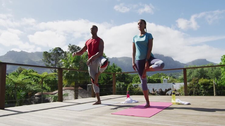 Relaxed biracial couple on terrace, practicing yoga together on mats