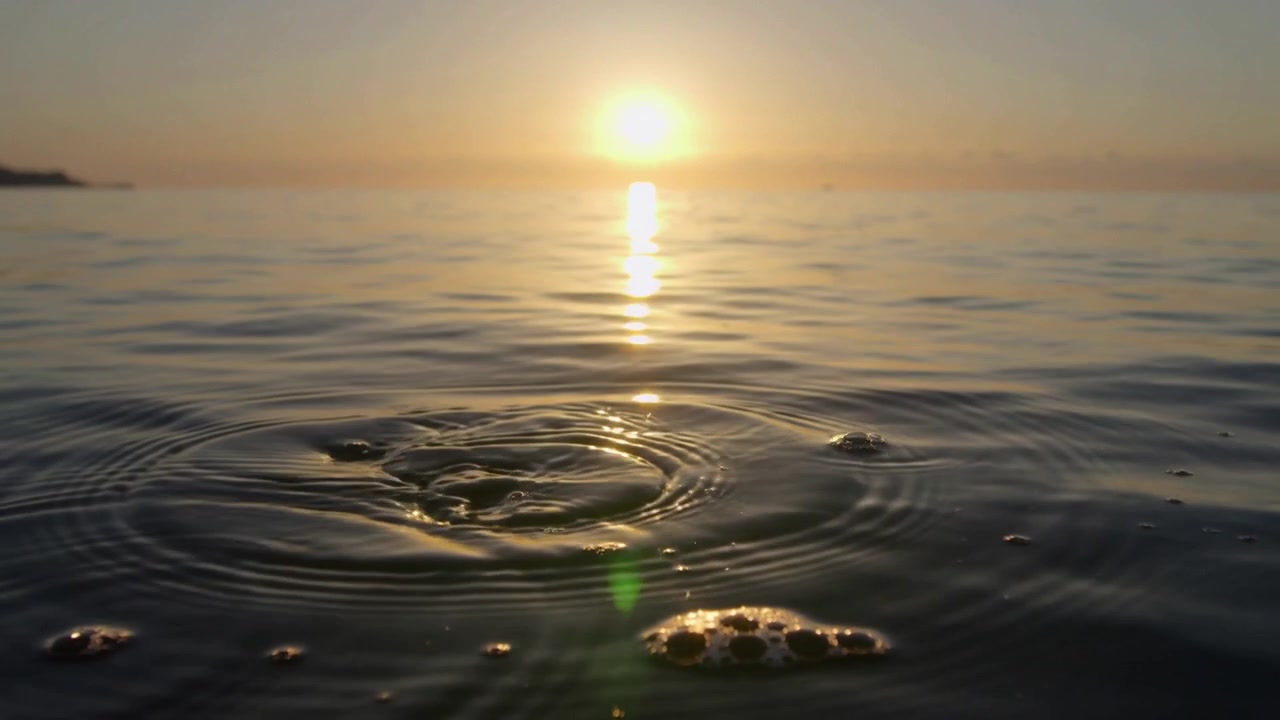 Rippling water forming concentric ripples after bubble breaking at coastal sunrise, sun reflection