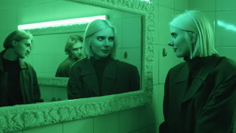 young woman and man looking in mirrors in room with green light