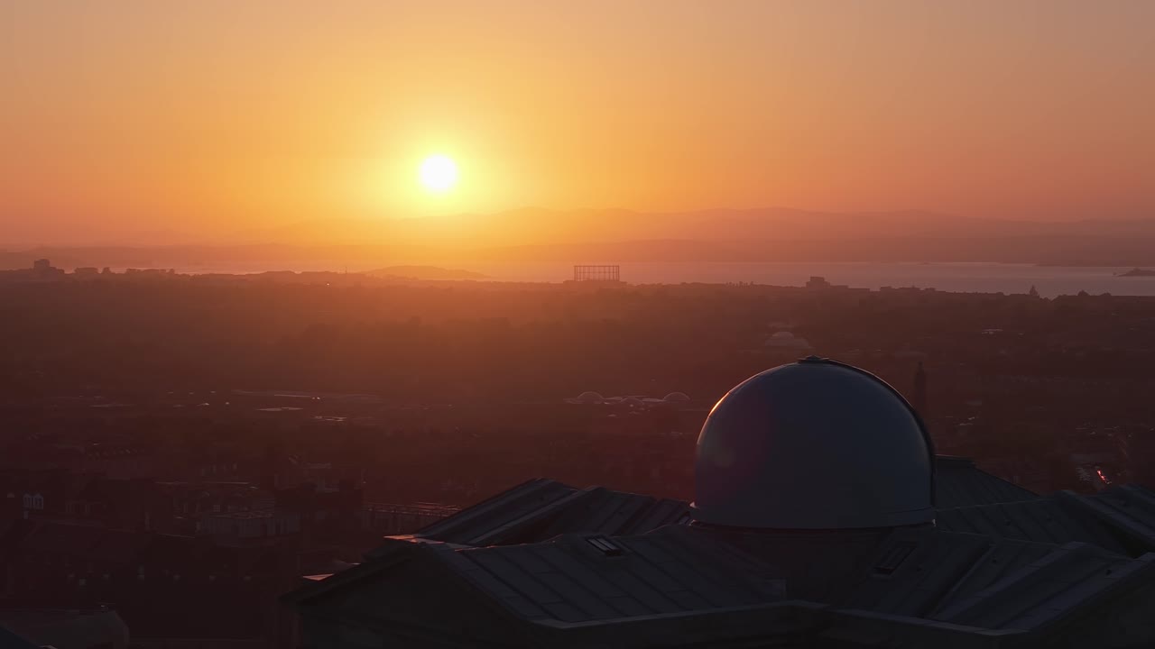 Cinematic drone orbit at sunset from Calton Hill, showcasing Edinburgh's skyline, historic monuments, and warm golden light across the city