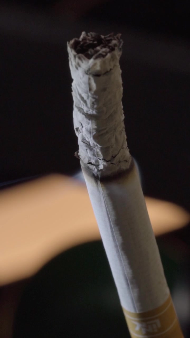 Closeup of burned cigarette tip showing loose ash and charred tobacco. Detailed paper texture and dark background create a dramatic macro view of the cigarette.