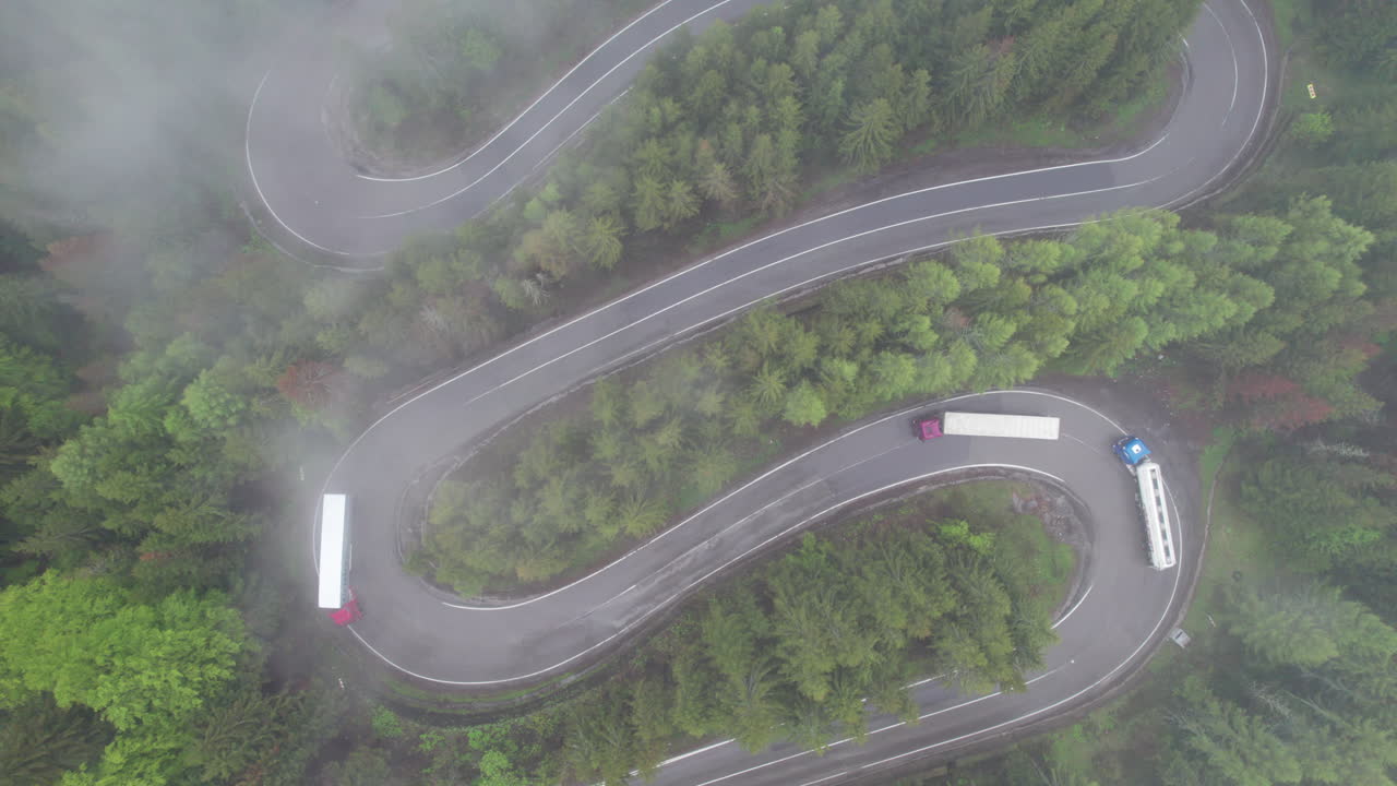 Aerial view of trucks driving on winding road in Romania covered by clouds